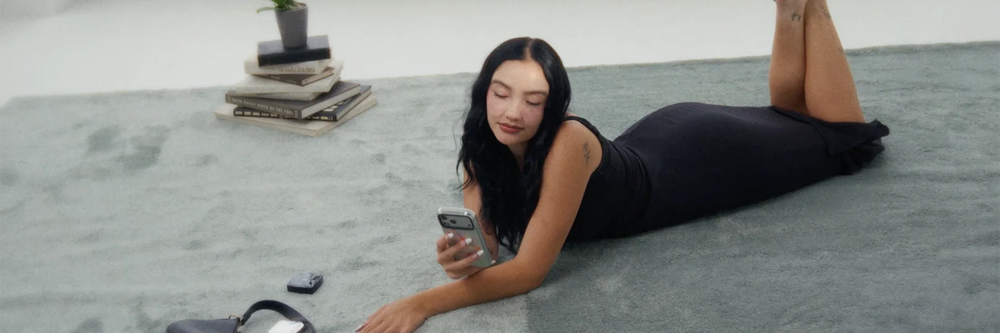 A model relaxing on a rug, using her phone in a reflective KELAB chrome case
