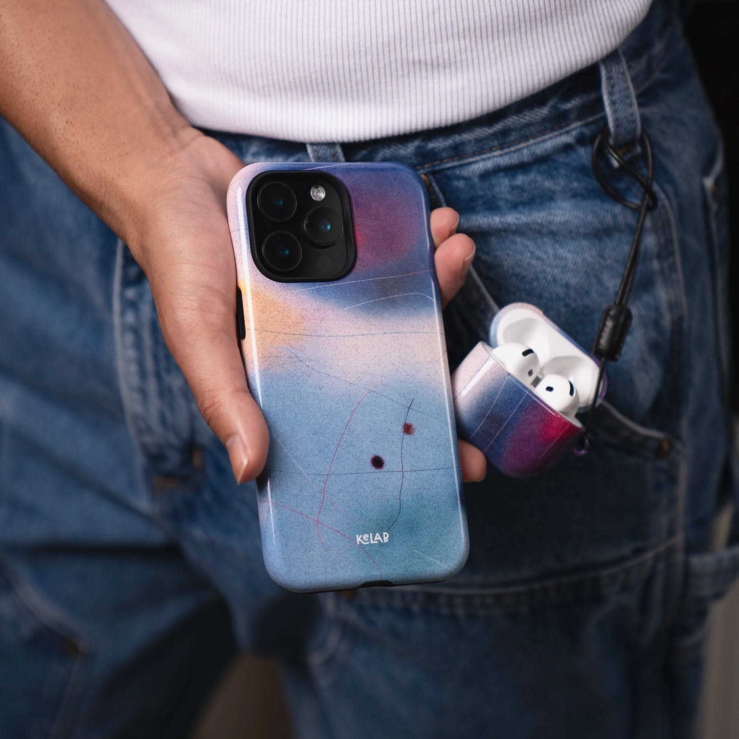 Cute AirPods Case in Blue from KELAB's Endorphins Series shown clipped to jeans, matching a gradient phone case held in hand. Stylish and protective.