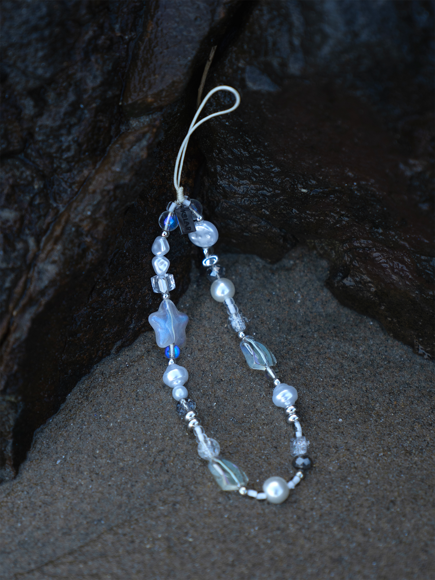 Cosmic Pearl Phone Charm – Star & Pearl Aesthetic by KELAB, featuring iridescent beads, frosted star, and silver accents on sandy beach backdrop.