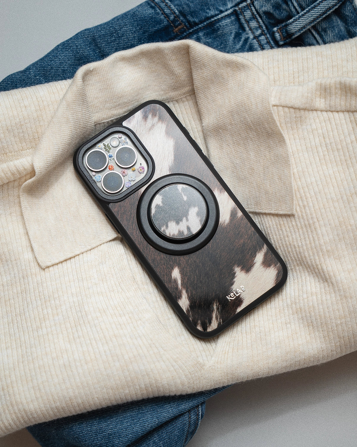 KELAB brand cow pattern Phone case with pop socket on a beige fabric background