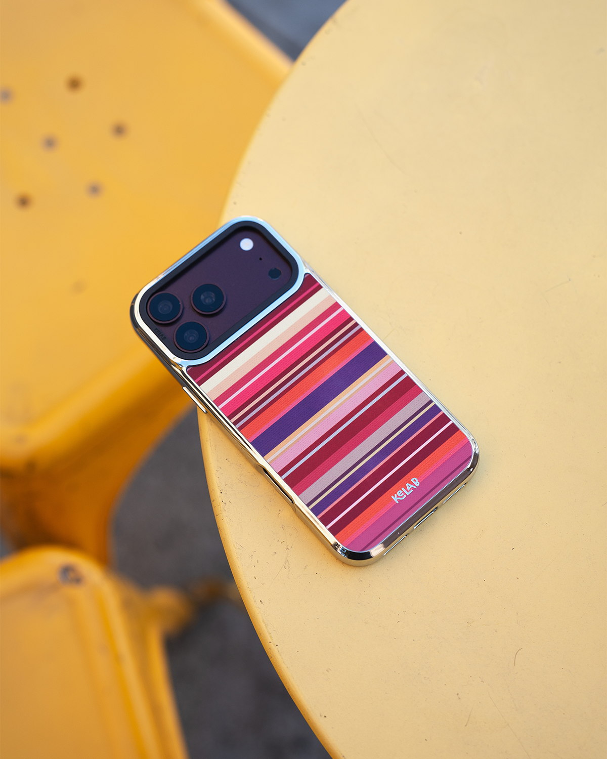 Warm Red Multi-Stripe iPhone case, angled lifestyle shot on a cafe table