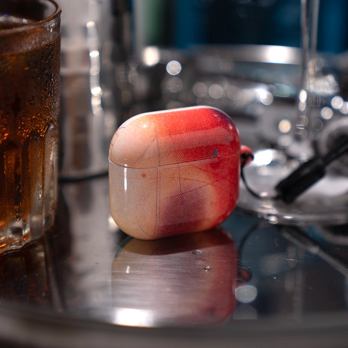 Climax Endorphins Series AirPods Case in red gradient by KELAB on a reflective surface beside a cold drink. Stylish and protective for all AirPods models.