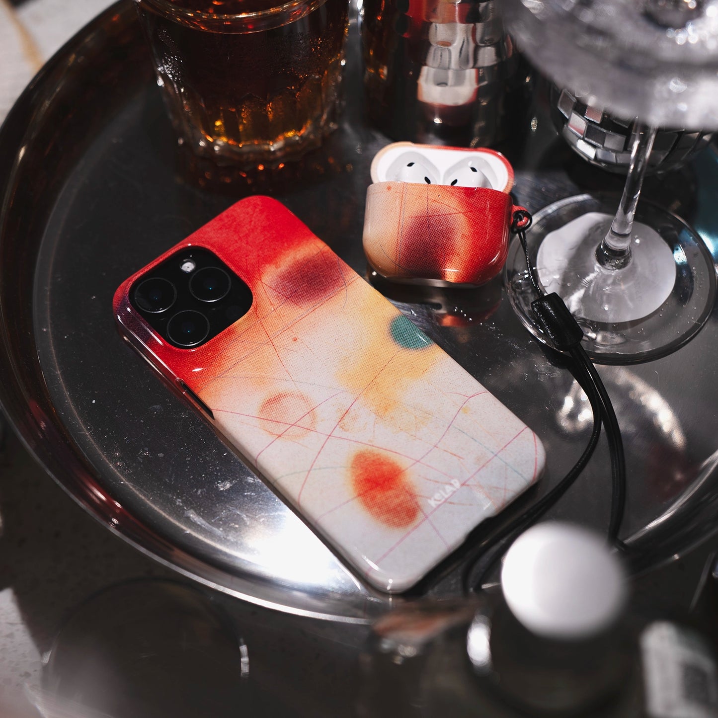 Endorphins Series - iPhone Case Bold for iPhone 16 Pro Max shown with matching AirPods case in vibrant red-orange gradient on a silver tray.