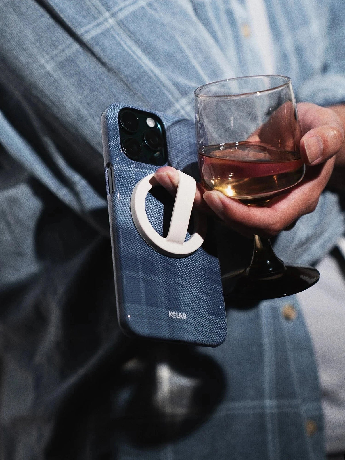 KELAB blue flannel iPhone case in lifestyle setting, paired with a grip accessory and drink, showcasing its casual plaid design and functionality.
