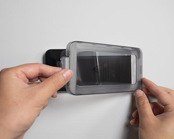 A person using an easy install tray to apply a screen protector to a smartphone.